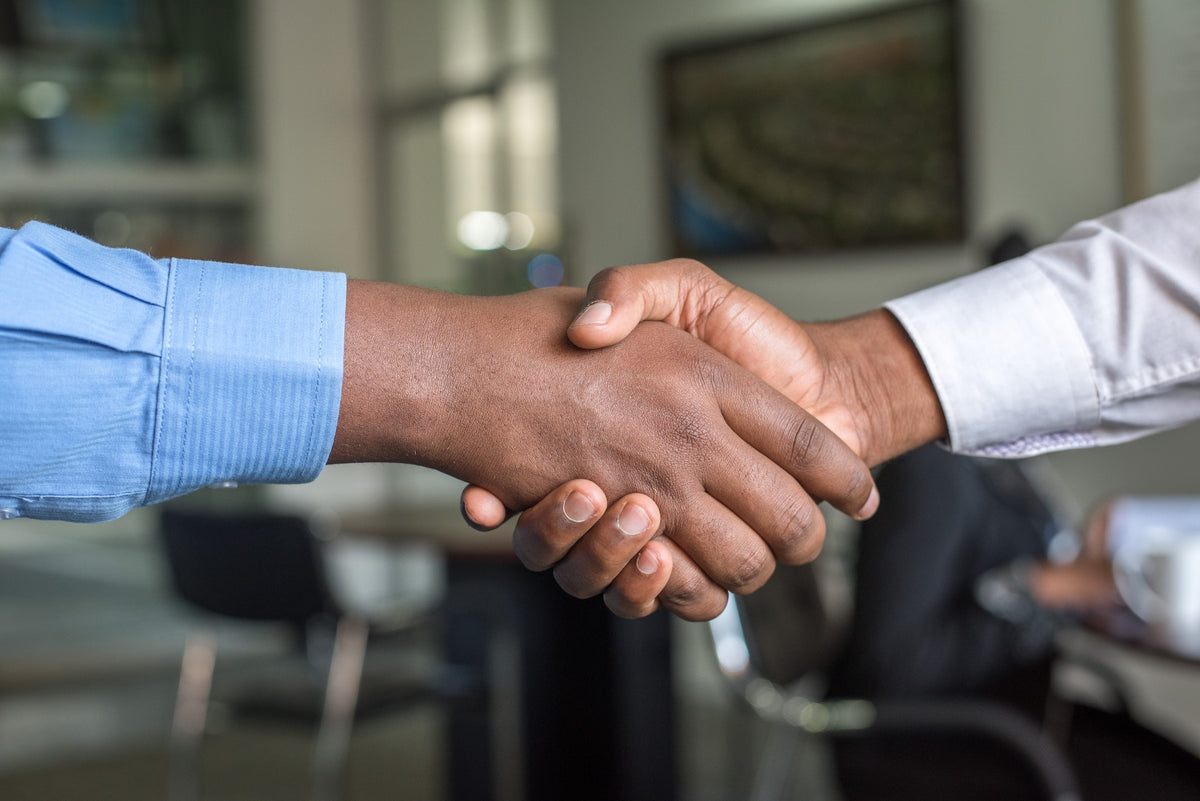 Two people shaking hands in an industrial setting with a factory in the background.